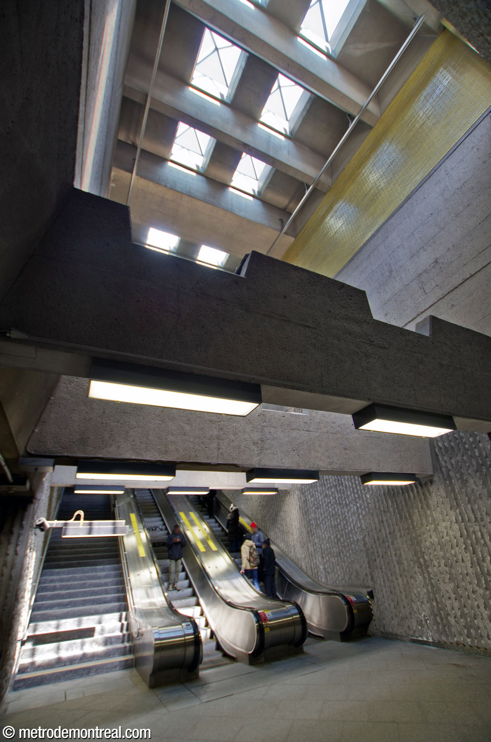 Le pied des escaliers vers la sortie Hochelaga Sud. Le volume impressionnant de la cage d'escalier est articulé par des poutres en béton crénelé. On voit au plafond les lanterneaux qui l’illuminent.
