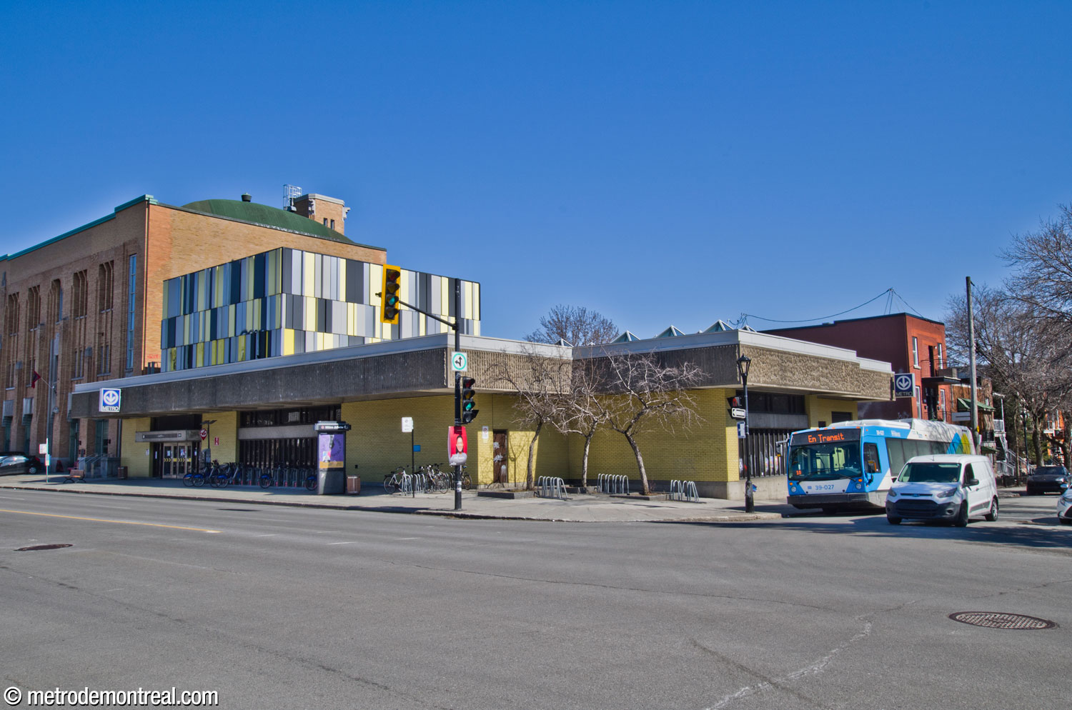 Vue d’ensemble de l’édicule Hochelaga Sud, à travers le carrefour des rues Hochelaga et Joliette. On voit sur le toit les lanterneaux pyramidaux (droite), ainsi que le local technique ajouté au toit en 2018-2019, dont l'intégration architecturale laisse à désirer.