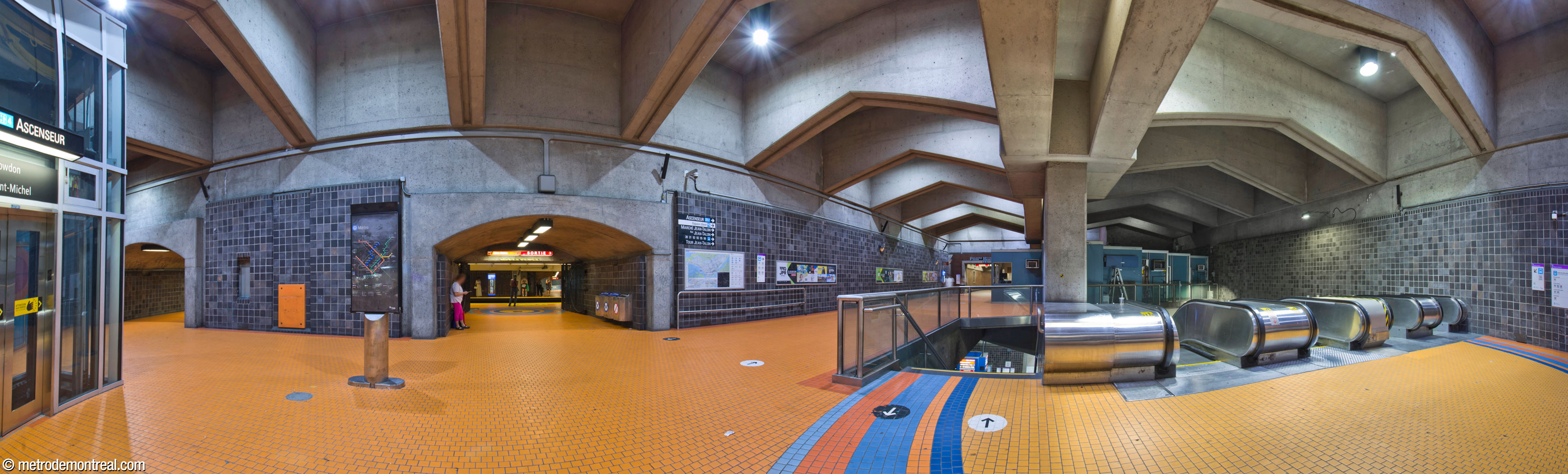 Le niveau supérieur de la galerie ouest. À gauche, deux tunnels relient ce niveau au quai Côte-Vertu. Au centre au fond, un couloir mène jusqu'au pied de l'escalier vers la billetterie. À centre droite, un local est aménagé pour le personnel de station derrière les escaliers vers la ligne bleue. L’ascenseur vers la ligne bleue est à l’extrême gauche.