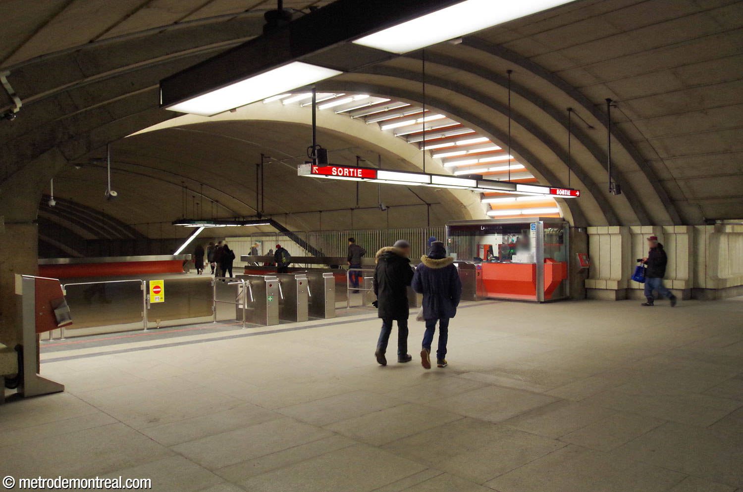Vue de la ligne de perception, située sous une arche illuminée. On regarde vers la zone contrôlée de la mezzanine.