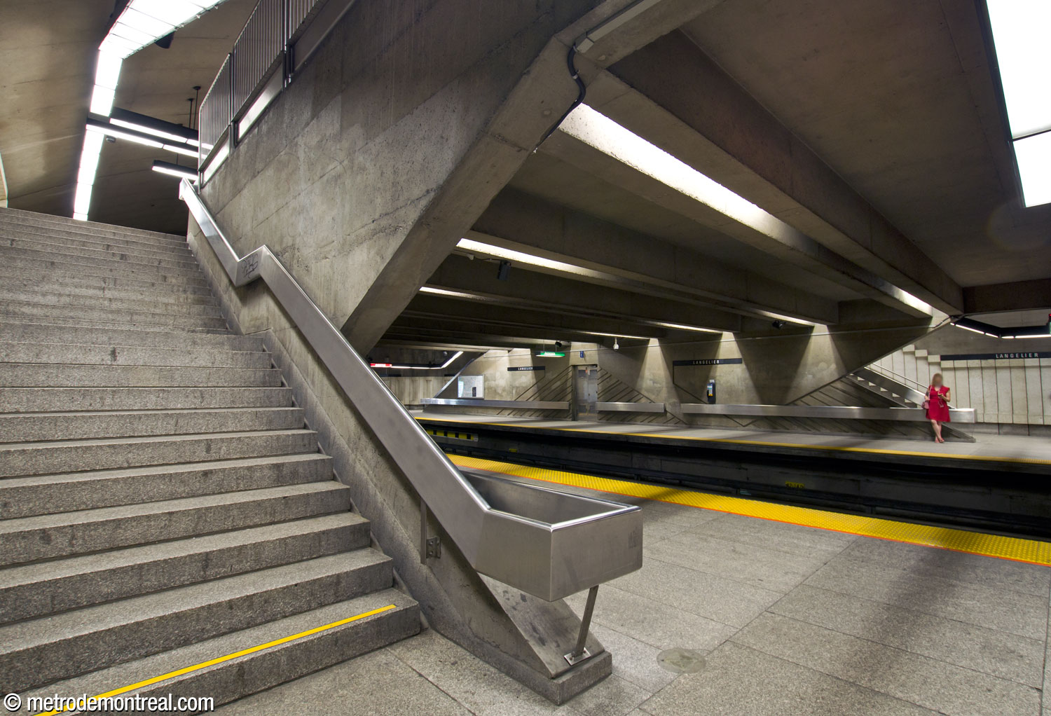 Dans cette vue d’un escalier vers le quai Angrignon, on voit au fond, sur le quai opposé, l’un des murs distinctifs situés entre les escaliers vers la mezzanine. Cette perspective montre comment ce dernier reprend l'angle du parapet et des escaliers.