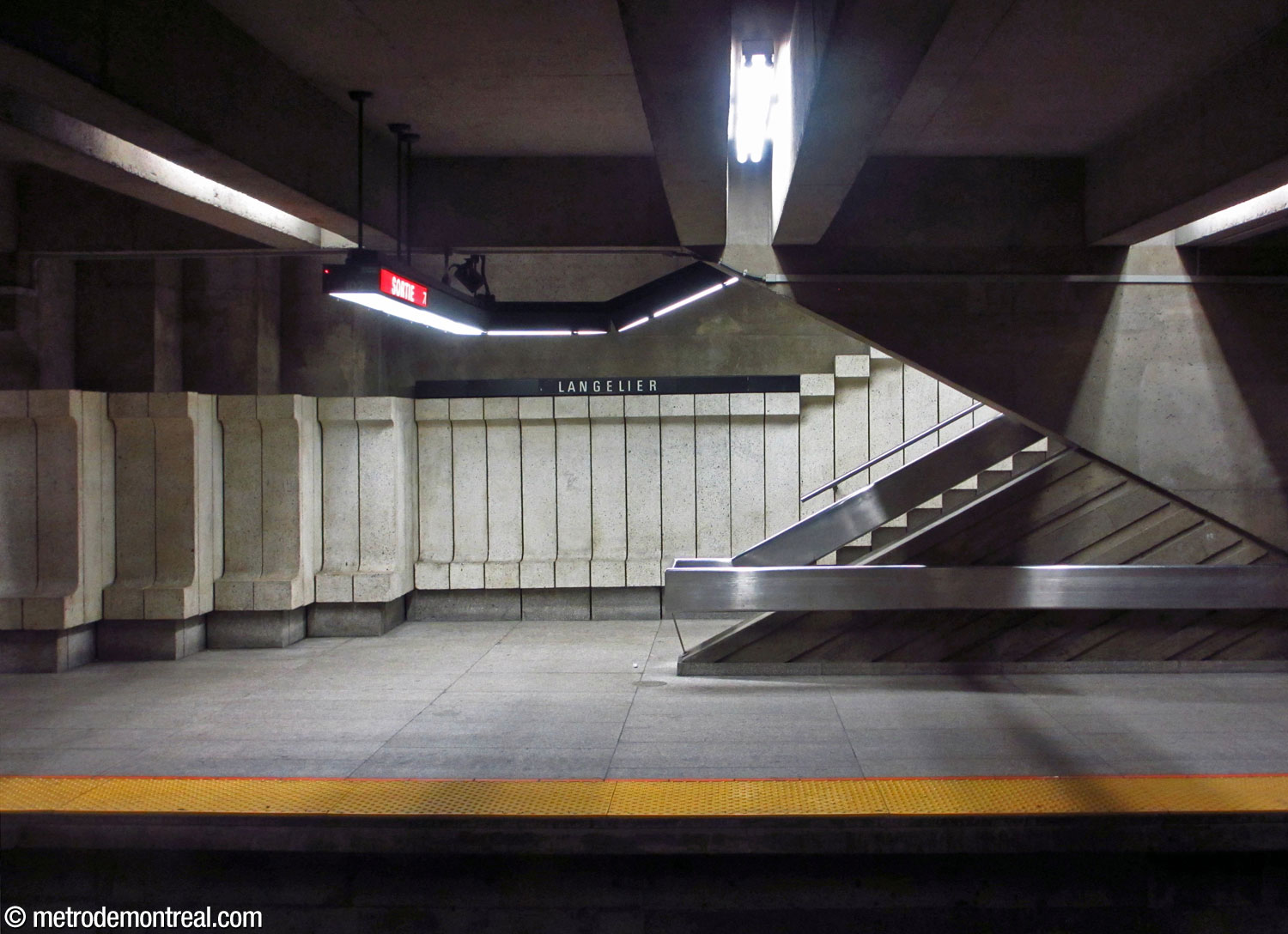 Le pied de l'un des escaliers vers la mezzanine, paré des modules muraux en béton; à droite, les angles de l'un des murs centraux.