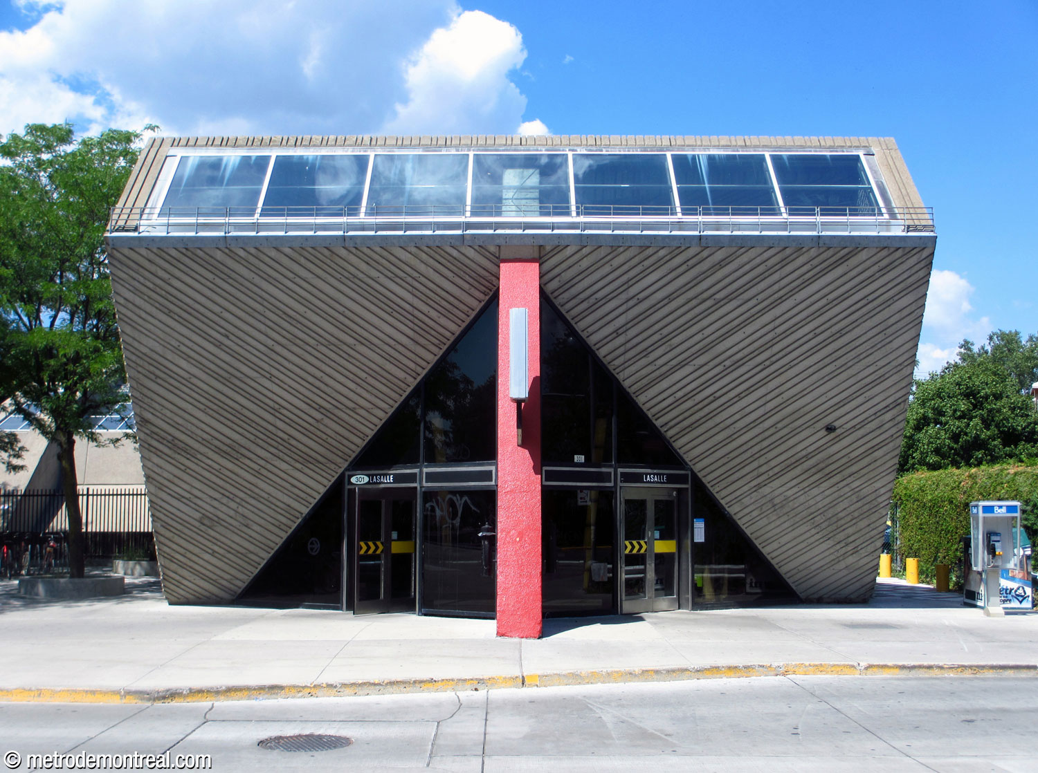 Front view of the station's headhouse. The triangular glass walls incorporating the entrance doors protrude forward on either side of a central red form.