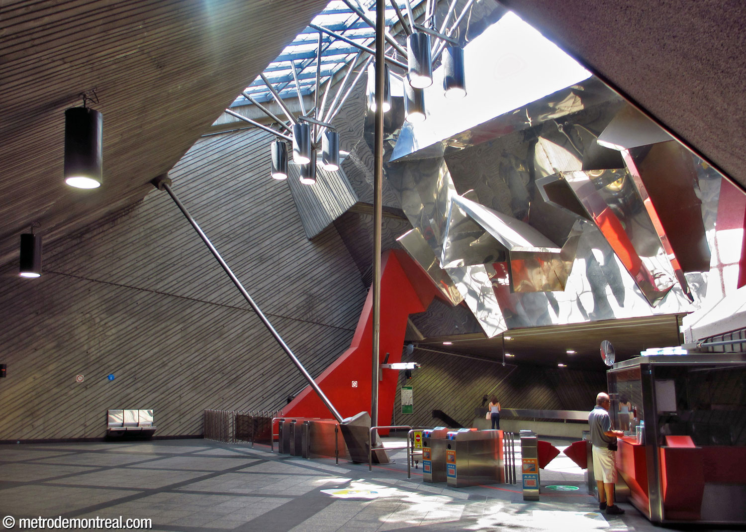 Overview of the mezzanine hosting the ticket hall. Overhead, a light shaft illuminates a mural sculpture by Peter Gnass, which spreads the sunlight throughout the space. The mezzanine is partly supported by the two long rods at centre connecting it to the roof.