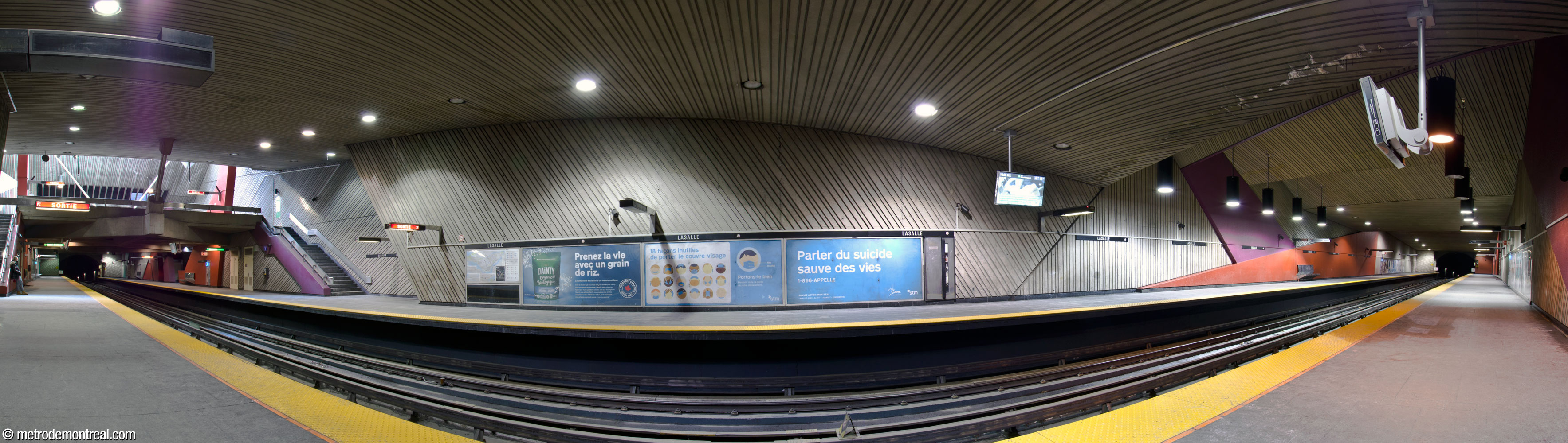 A panorama of the station's trainroom taken from the Honoré-Beaugrand platform, showing the station’s irregular walls, reeded concrete, large coloured masses, and sunlit ticket hall mezzanine (left).