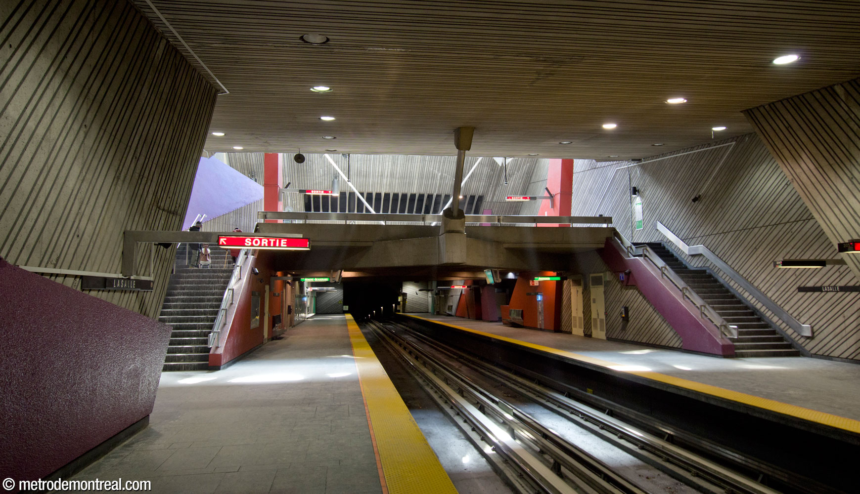 View of the mezzanine over the tracks and the stairs connecting it to the platforms, with sunlight from the light shaft illuminating the platforms.