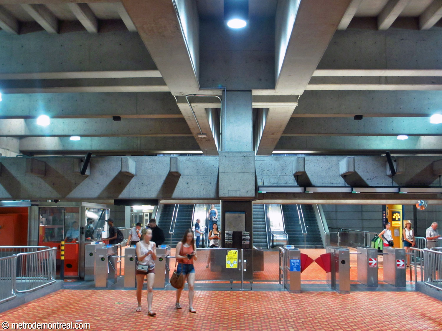 La billetterie de la station située au niveau de la mezzanine au-dessus des quais. En arrière, on voit les escaliers vers la sortie. En haut, une paire d’immenses poutres articulent l'espace.
