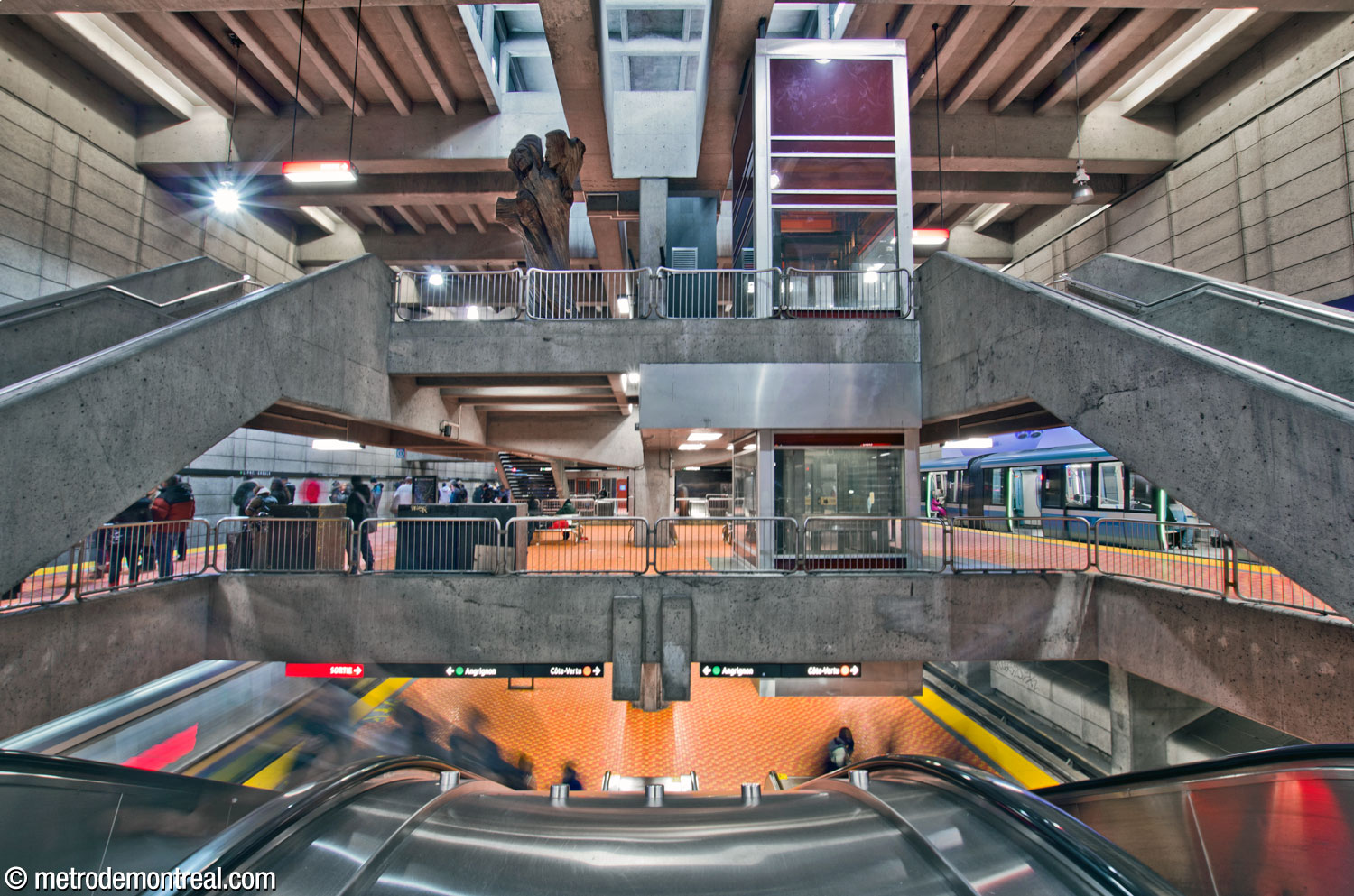 Vue vers l'est à partir du quai supérieur. On voit le grand volume et tous les trois niveaux de la station. En haut on voit l'un des puits de lumière qui illuminent le volume. Au-dessus des quais, la mezzanine accueille la sculpture L'Arbre de vie de Joseph Rifesser, qui trône à côté de l'ascenseur reliant la mezzanine et le quai supérieur.