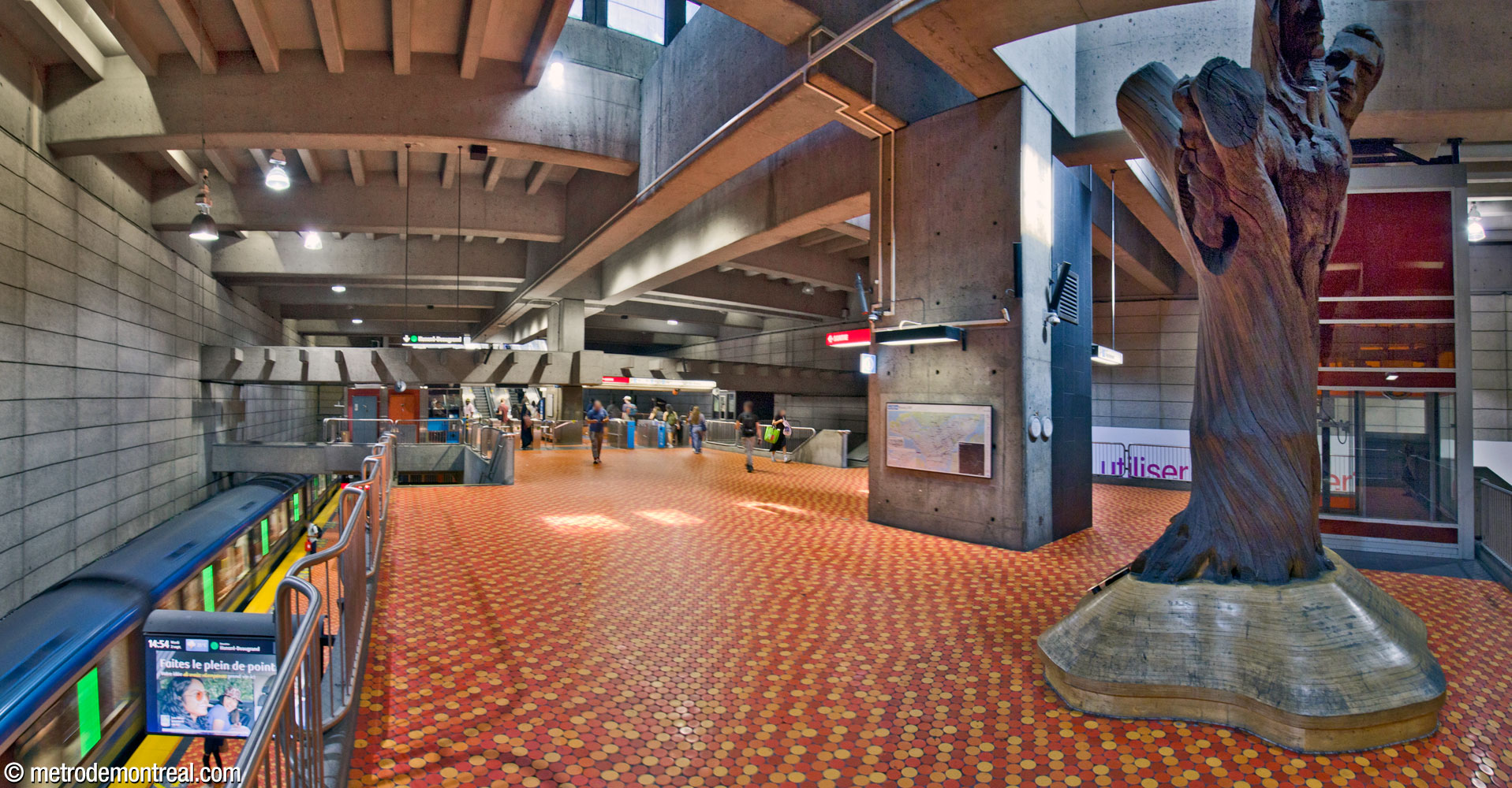 Vue d’ensemble de la zone contrôlée de la mezzanine. Les parapets de chaque côté de la mezzanine donnent sur les voies du quai supérieur (gauche). À droite, la sculpture L’Arbre de vie de Joseph Rifesser se tient au bout de la mezzanine, à côté de l’ascenseur vers le quai supérieur.