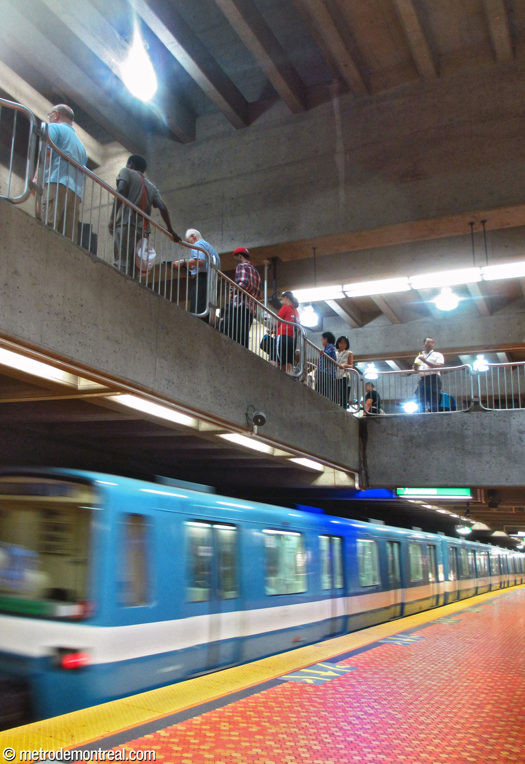 Vue vers le haut à partir du quai inférieur. Un train en direction Angrignon arrive au quai inférieur, en passant sous le bord du quai supérieur.