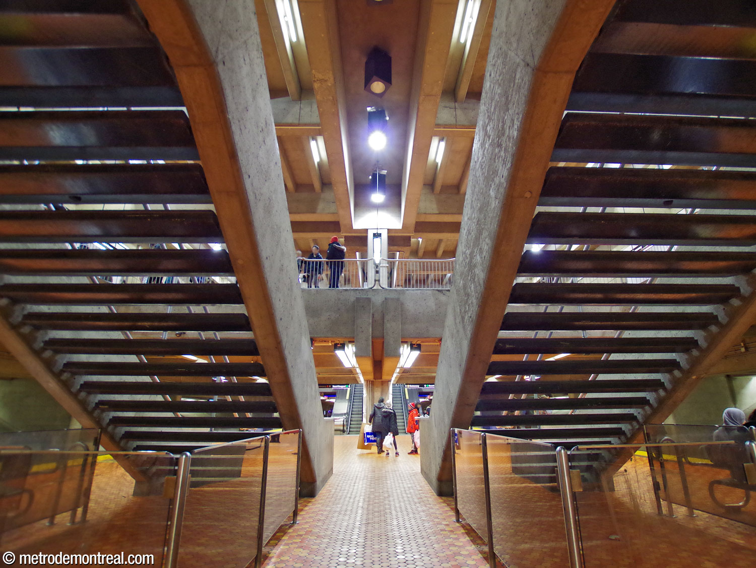 Vue entre les escaliers à l'extrémité ouest du quai inférieur. Les escaliers fixes reliant les deux quais et la mezzanine sont dépourvus de contremarches, créant une transparence qui rajoute à l’impression que les différents étages flottent en apesanteur dans le volume de la station.