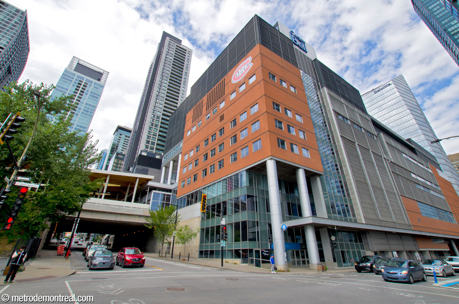 The southwest corner of the Bell Centre rises over Rue Saint-Antoine. At the corner, an entrance provides access to the commuter train station. The viaduct carrying the tracks is seen above Rue de la Montagne at left.