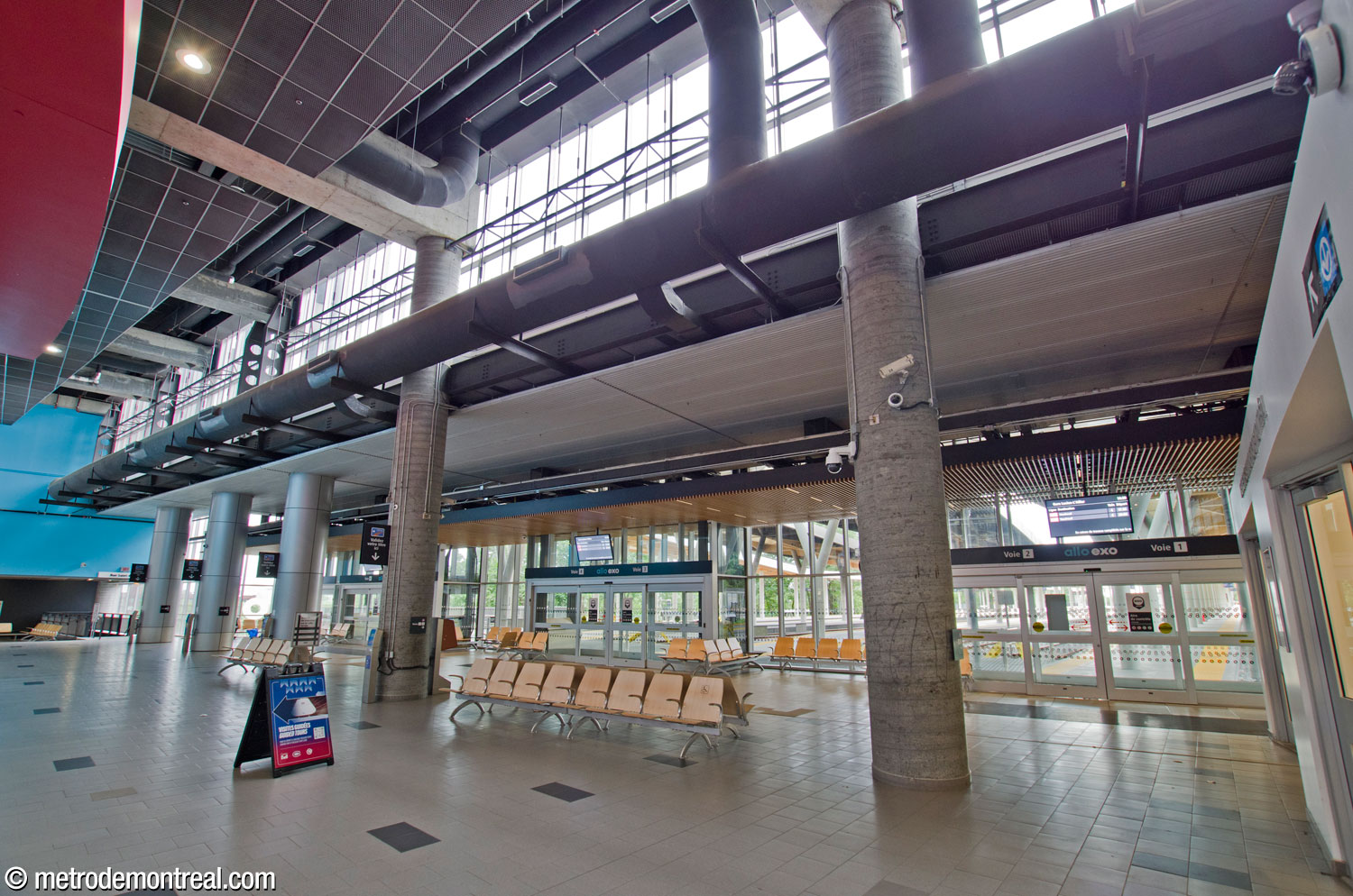 Looking south along the length of the commuter train station interior, toward the ticket booth and Rue Saint-Antoine exit. The two-storey space features exposed columns and ductwork and additional daylight is provided by clerestory windows. At left is a Montreal Canadiens souvenir store.