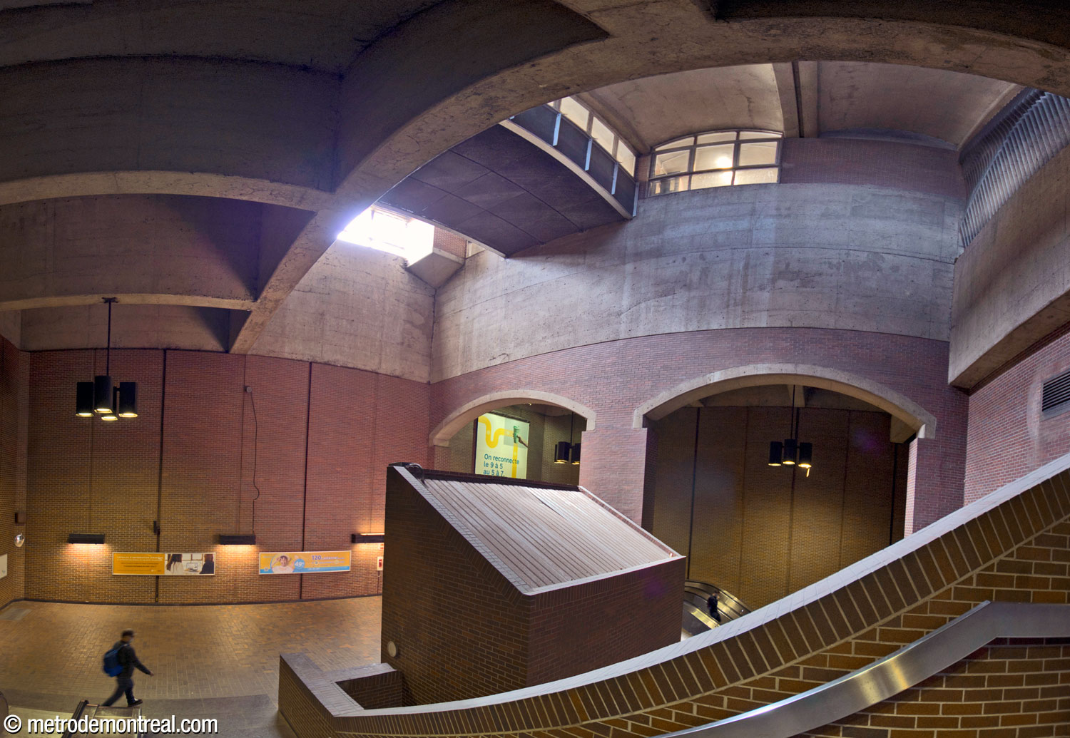 Panorama looking down on the second landing and the volume above it, seen from the stairs coming down from the first landing. Above, the volume admitting light and ventilation from the surface is crossed by a glassed-in bridge connecting the headhouse entrance with the passage to the commuter train station. The headhouse overlooks the volume through the windows nearby. Above right, the mouth of a ventilation shaft is camouflaged by a sculptural grille by Jean-Jacques Besner. In the background, the stairwell to the ticket hall is separated from the main volume by large archways.