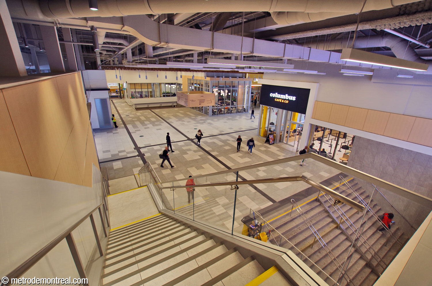 View of the lobby inside the residential complex constructed on top of the metro station. The stairwell down to the ticket hall is at bottom right; the one in the centre background comes up from the arrival platform. The passage at centre left leads outside to Place Charles-Le Moyne; the one at upper right leads to the bus terminal. The staircase from which the photo was taken leads up to the overhead walkway leading to Édifice Port de Mer.