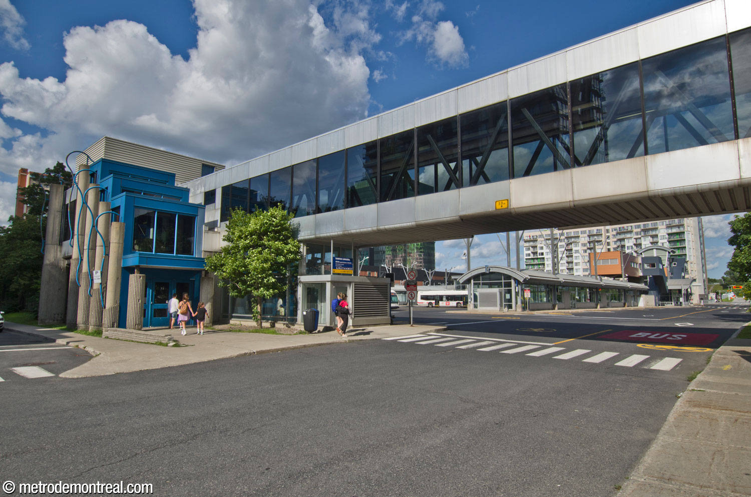 At the southwestern corner of the Longueuil bus terminal, a skywalk leads to Complexe Bienville. Wavy blue forms decorate the sides of the building near the entrance.
