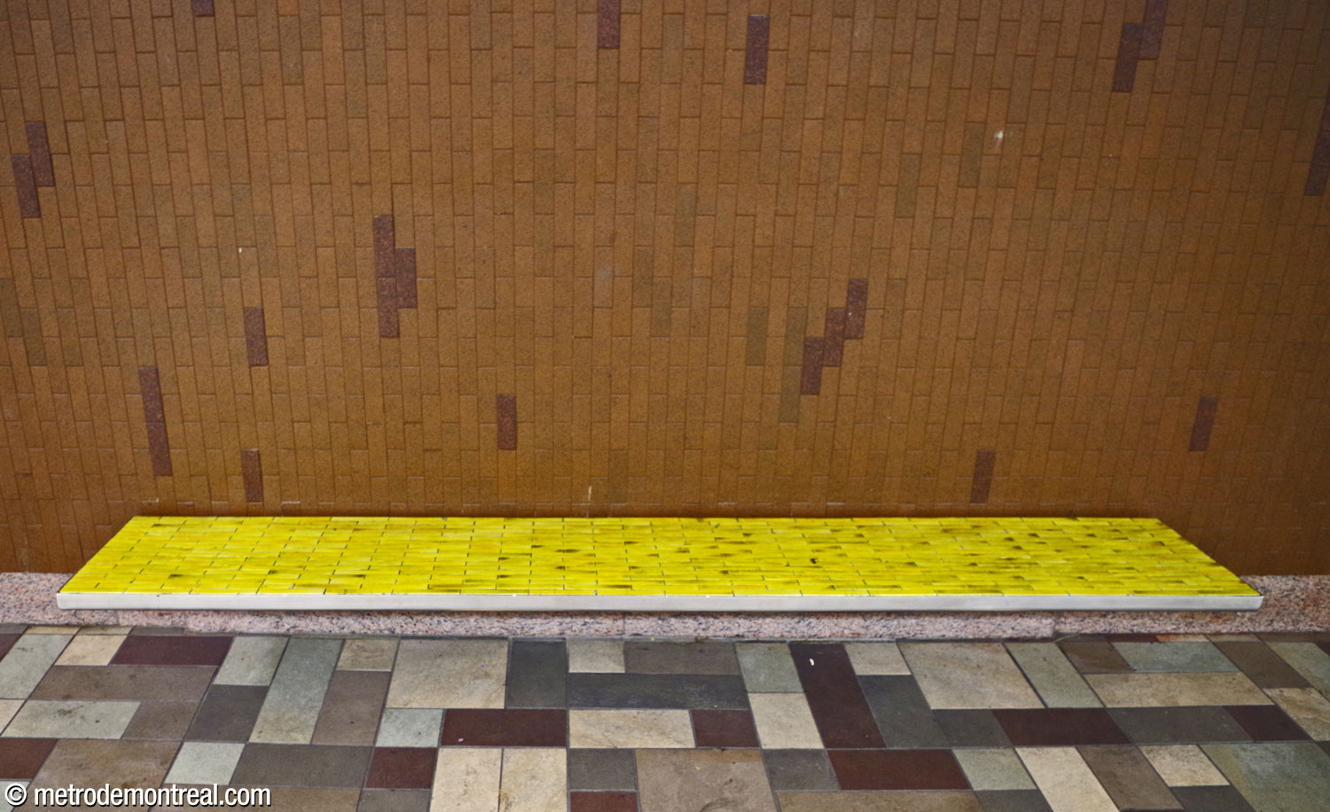 The station's benches are clad in yellow glazed ceramic tiles. The portions of the walls not clad in travertine are in vertically set brown tiles punctuated by darker brown tiles standing out slightly from the surface.