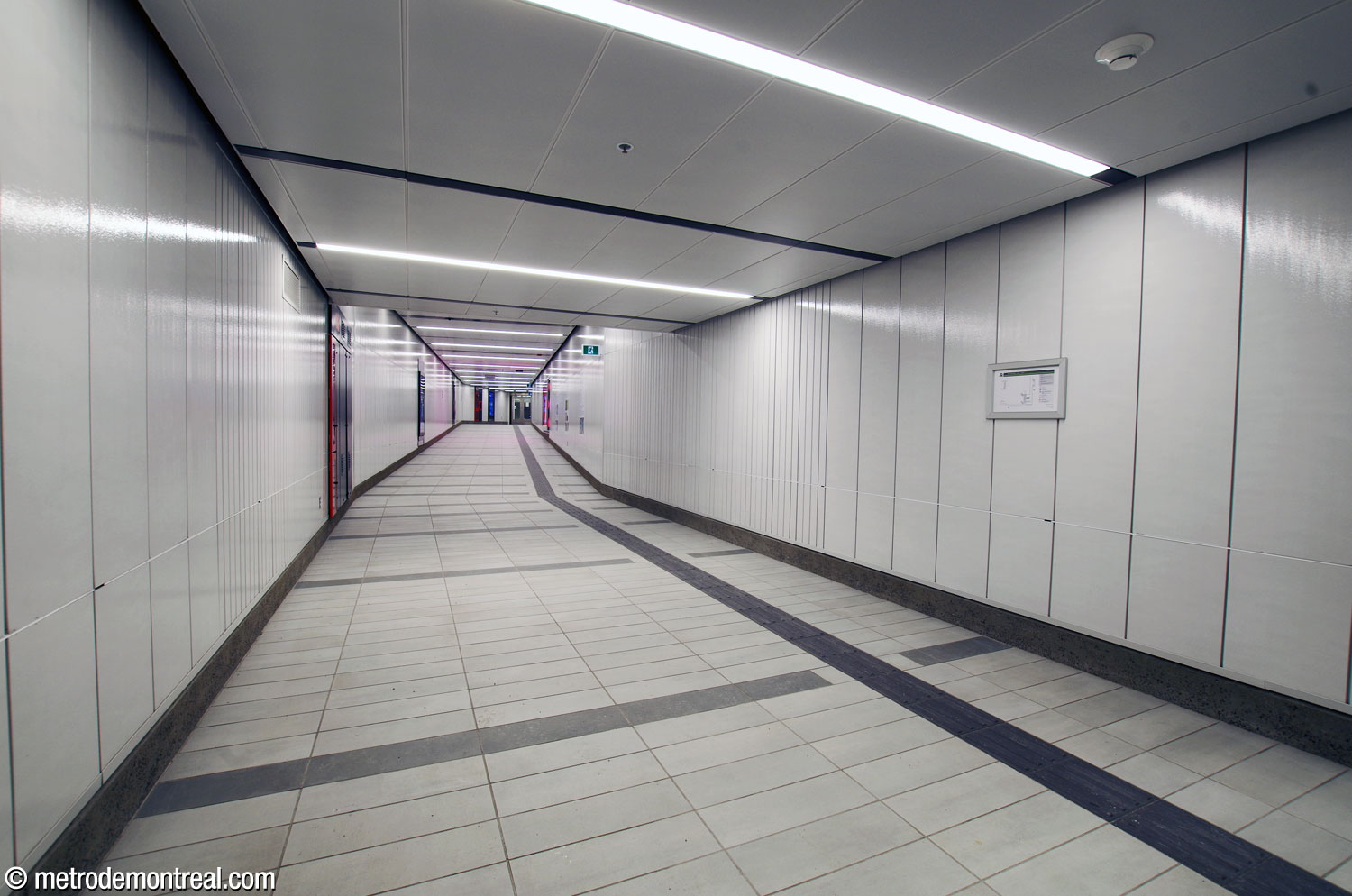 The passage from the metro to the north ticket hall of the REM station, about 60 metres long. The station’s white enamelled metal wall plates are placed vertically in the upper areas of the station.