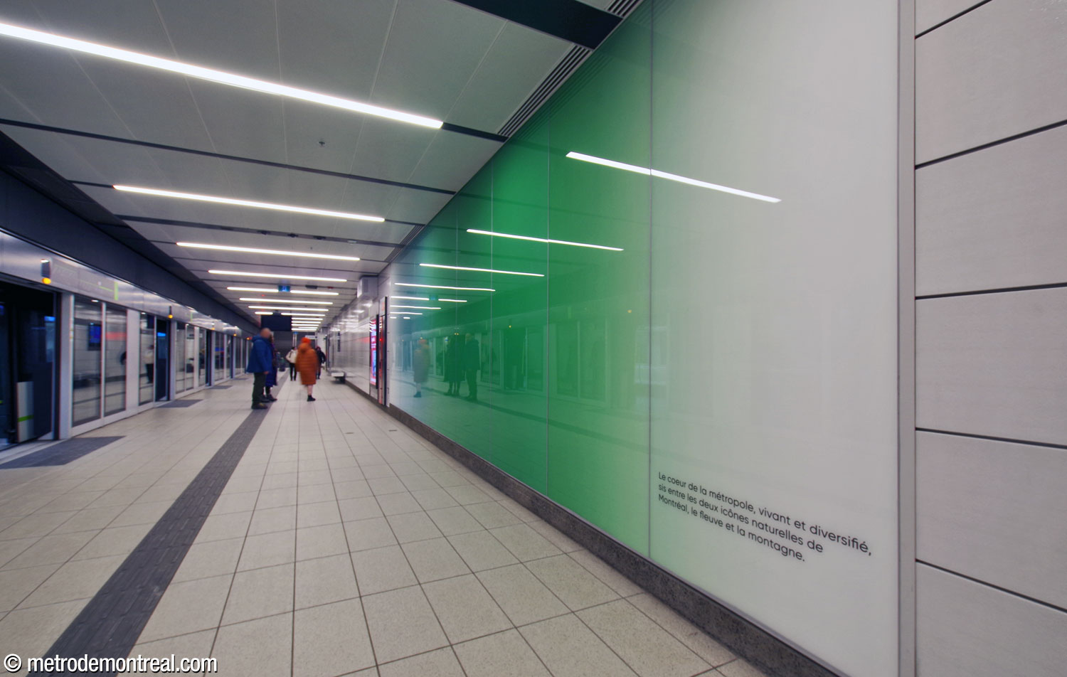 One of the station’s decorative gradient panels, this one white, green, and blue, located on the southbound platform. It features text describing the station’s location and the inspiration for the colours of the gradient: “The heart of the metropolis, living and diverse, located between Montreal’s two natural icons, the river and the mountain.”