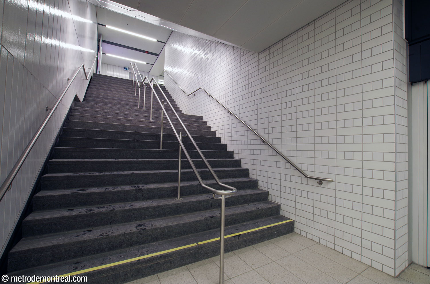 The stairwell from the end of the southbound platform up to the north ticket hall. The walls of the lower stairwells feature decorative ceramic tiling in a distinctive pattern of matte and gloss, as at other REM stations.