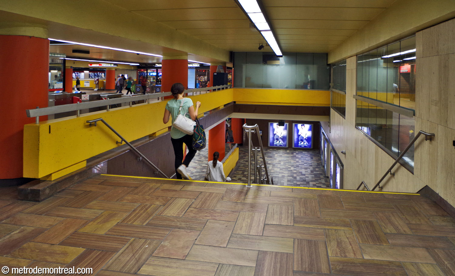 The stairs between the western ticket hall and the Honoré-Beaugrand platform. A glass wall separates the control zone from the south passage, while a long barrier divides the bottom of the staircase from the platform.
