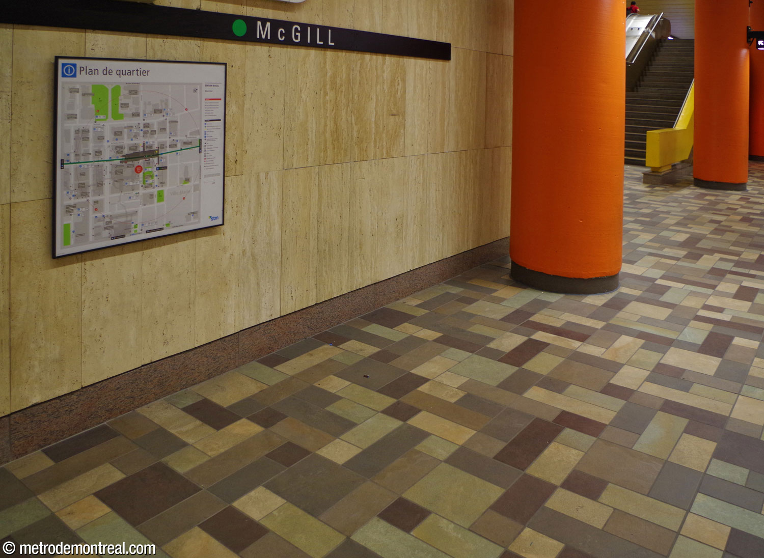 The station's finishings: cream-coloured travertine walls, earth-toned floor tiles on the platforms, and orange and yellow paint on the columns and barriers.