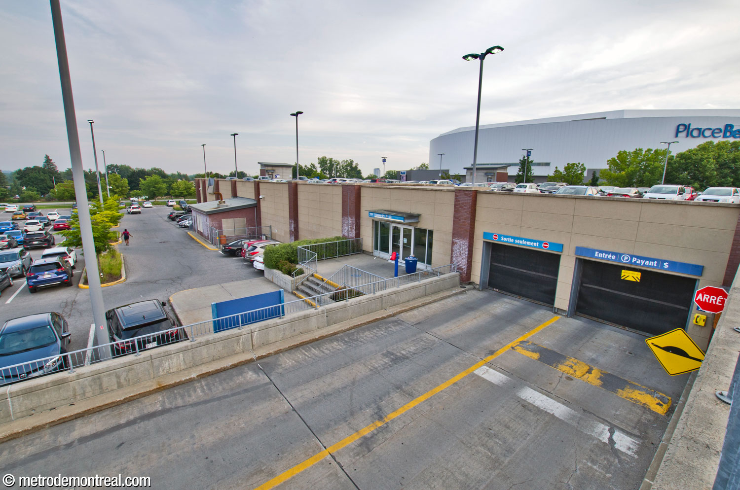 The driveways and pedestrian entrance to level P1 of the parking garage. In addition to the ground-level parking lots (left), outdoor parking is also visible on the roof of the garage (right).