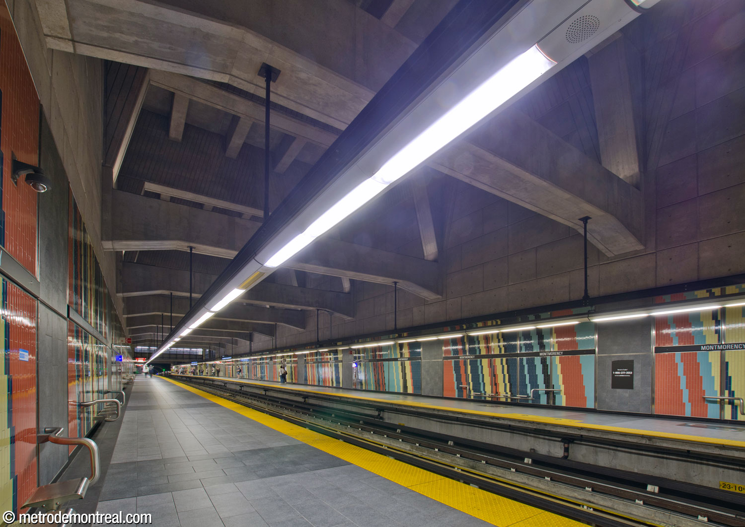 View of the platforms from the eastern end of the arrival platform. The main volume with its structural system is overhead; brightly coloured ceramic tiling lines the platform walls.