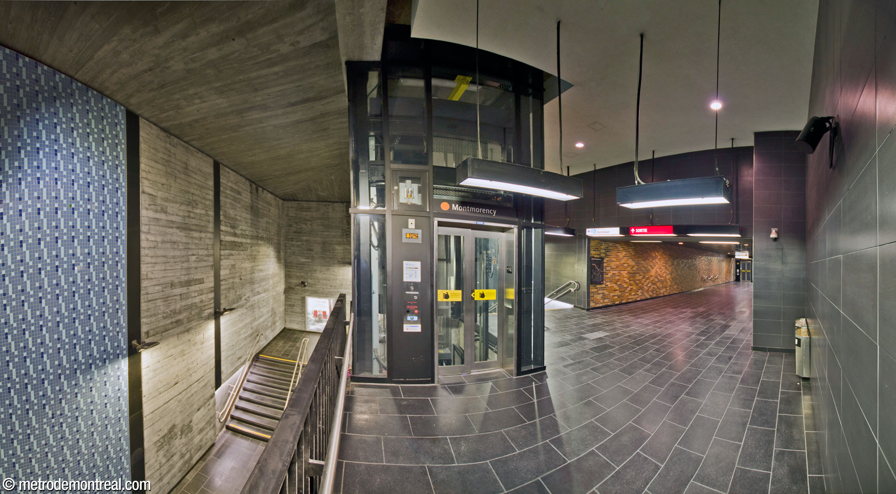 The landing at the upper level of the new access to the Montmorency platform. Facing the elevator access, a parapet overlooks the stairwell at left. At right is the crossing to the Côte-Vertu access and the stairs up to street level.