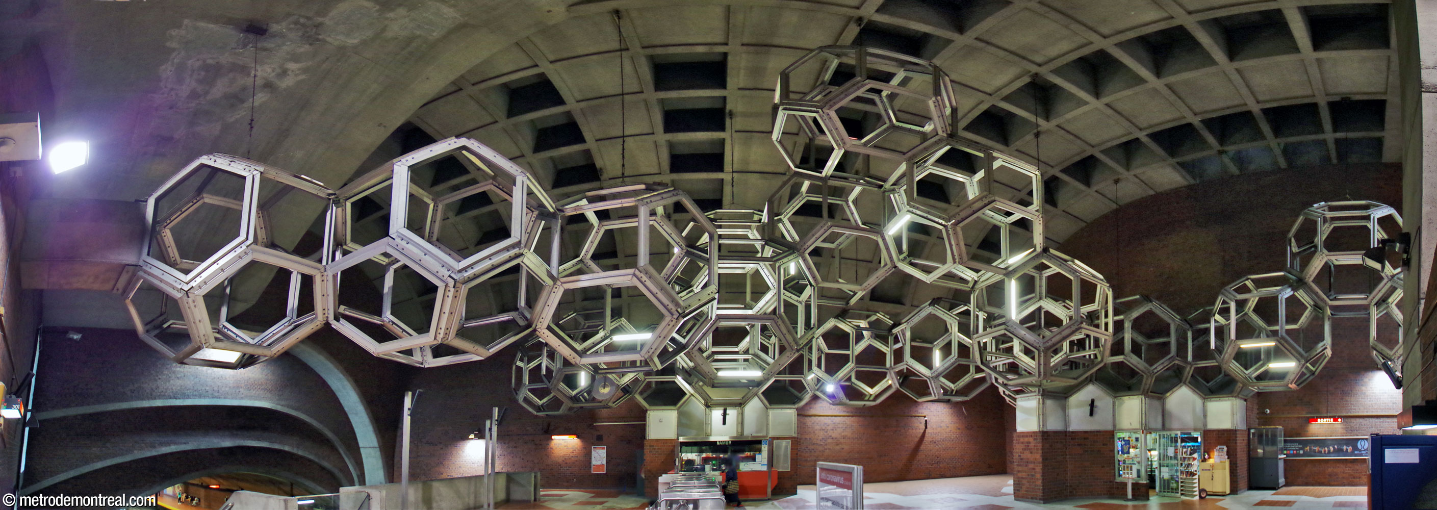 Panorama of Système by Pierre Granche, spreading through the main volume of the ticket hall, seen facing west toward the ticket booth. The sculpture is suspended from the roof, anchored to the walls, and supported by the roofs of the ticket booth and concession.