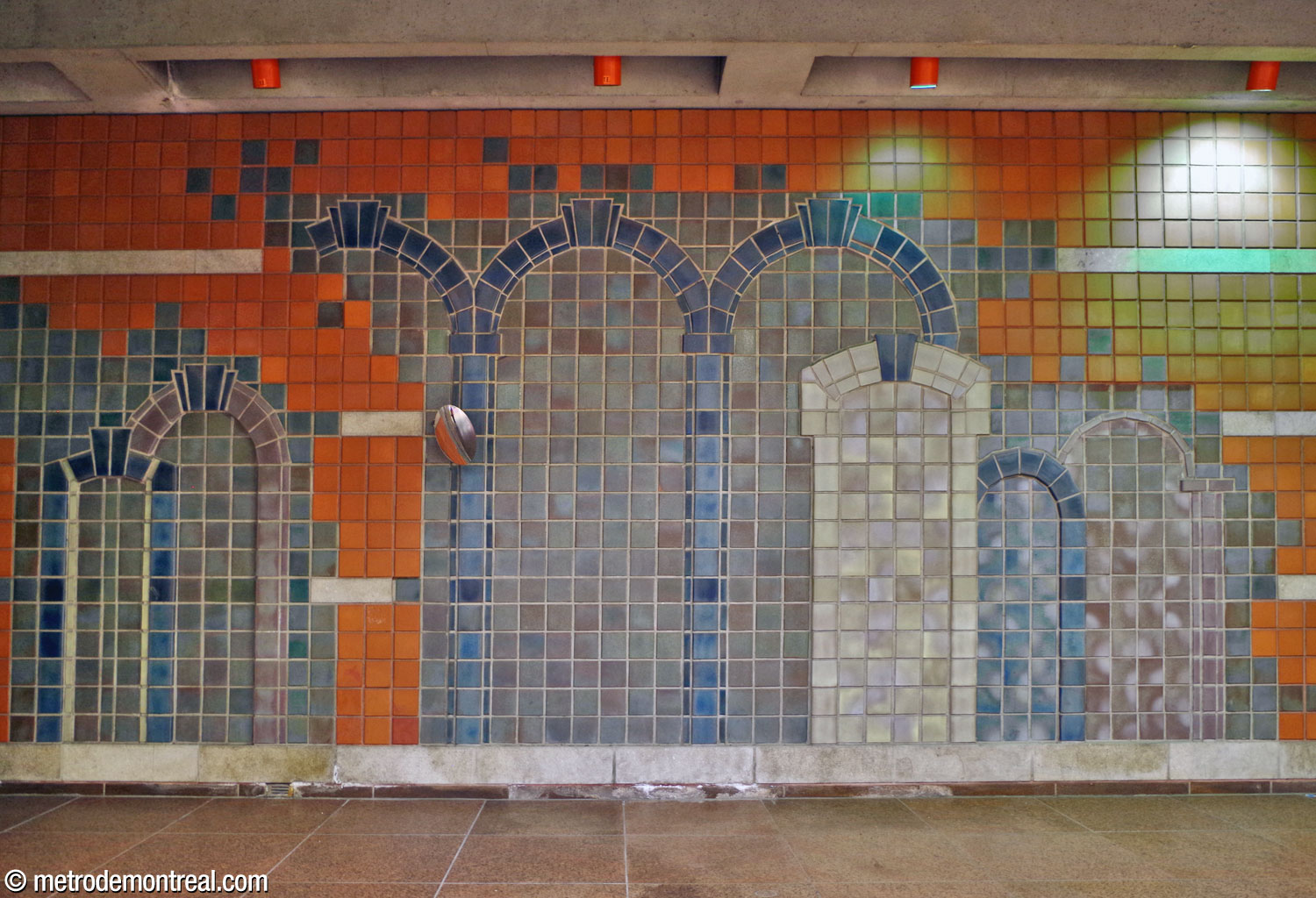 The largest section of the mural by Gilbert Poissant on the rear wall of the ticket hall, depicting typical architectural forms of doors and arches in Outremont. Its glazed sandstone tiles in shades of blue and grey are the same size as the station's terra cotta wall tiles and merge into them at the edges.