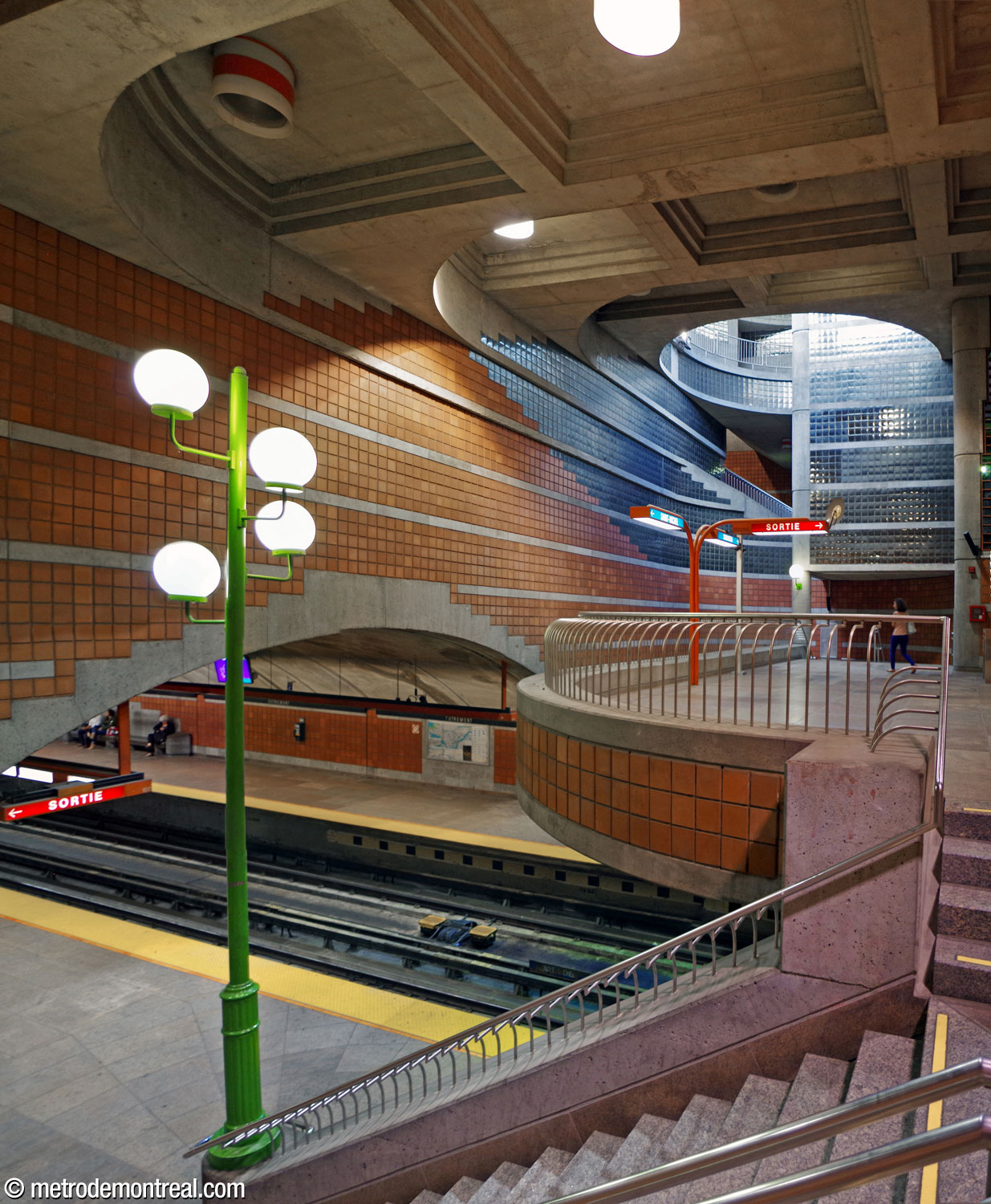 The main volume over the ticket hall mezzanine. Above, a stepped series of curves radiate out from the light shaft amid the square ceiling coffers. On the wall above the platform vault, the edges of the tiled sections are also stepped. Note the light fixture (left) standing atop the foot of the banister of the stairs to the Saint-Michel platform, whose pedestal is a City of Outremont lamppost.