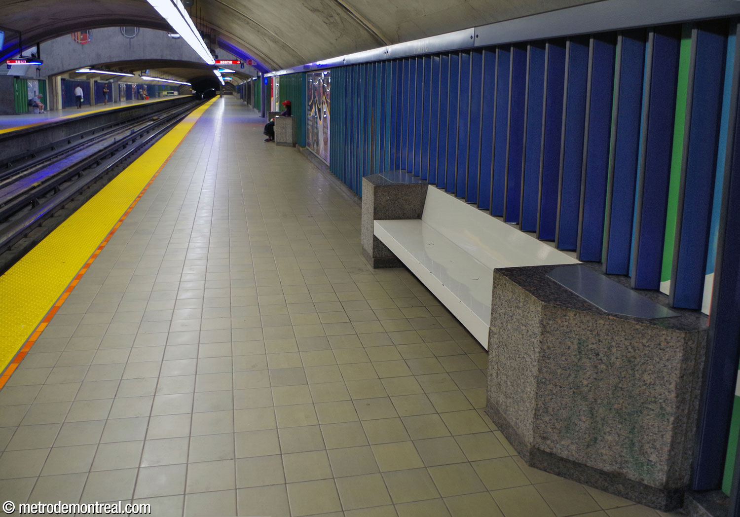 L'un des bancs du quai, de couleur blanche et encadré par des appuis de granit, ponctue la frise de Huguette Desjardins.