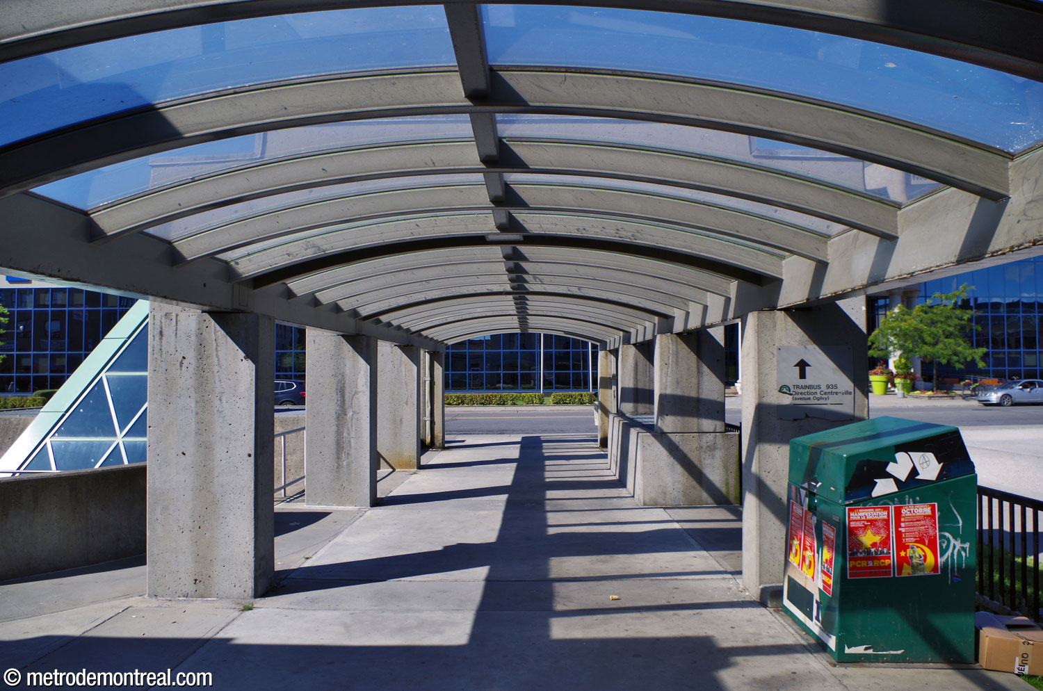 Vue intérieure de la pergola de béton menant vers la porte nord de la station de métro; on en voit la toiture transparente.