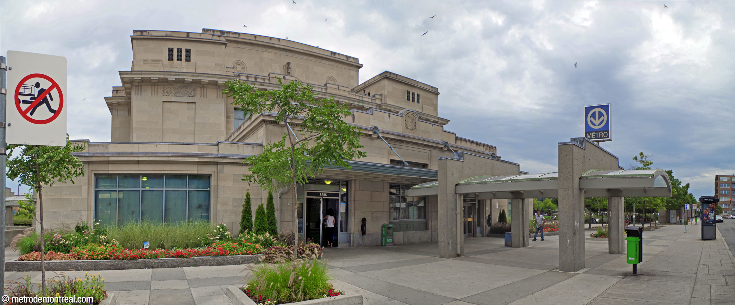 Vue oblique du côté ouest de la gare patrimoniale. On voit les entrées du métro et la pergola en béton (droite) qui les raccorde au trottoir.