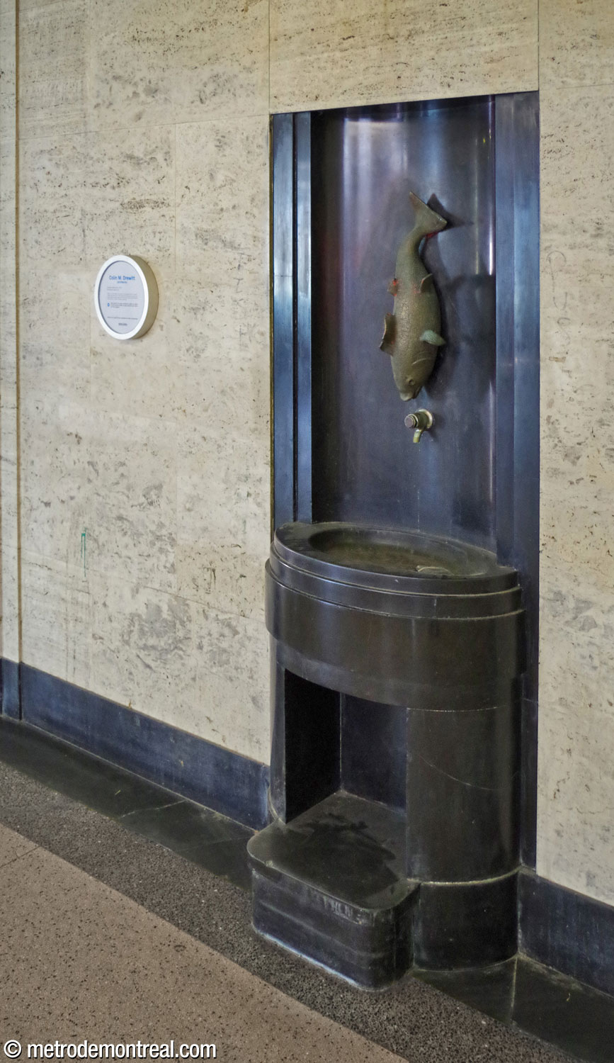 Une ancienne fontaine à boire en granite noir, ornée d'une sculpture élégante en laiton représentant un poisson, subsiste à sa position d'origine sur le mur est de l'accès au métro.
