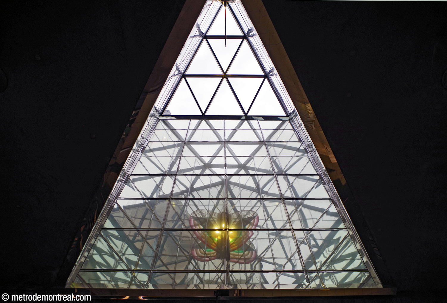 Le puits de lumière triangulaire au-dessus du pied des escaliers vers la sortie. On voit l'œuvre Métamorphose d'Icare de Claire Sarrasin au fond, reflétée dans les miroirs qui parent l'intérieur du puits; en fait, l'œuvre se trouve en haut de l'image.