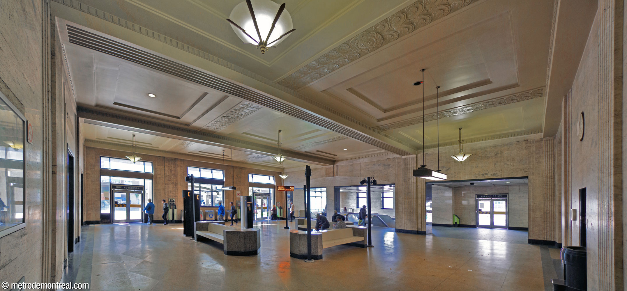 L'intérieur de l'entrée de la station, qui occupe l'ancienne salle d'attente de l'historique gare Jean-Talon. On regarde vers le nord-ouest; les portes se trouvent à gauche (rue Hutchison) et à droite (avenue Ogilvy). L'espace est revêtu de travertin beige pâle et exprime le style Art déco à travers plusieurs éléments décoratifs originels tels que les reliefs décoratifs au plafond et les planchers en terrazzo. De belles lampes restaurées en cuivre et verre, également de style Art déco, sont suspendues au plafond. Un groupe de bancs semblables à ceux des quais se trouve au centre de la pièce.