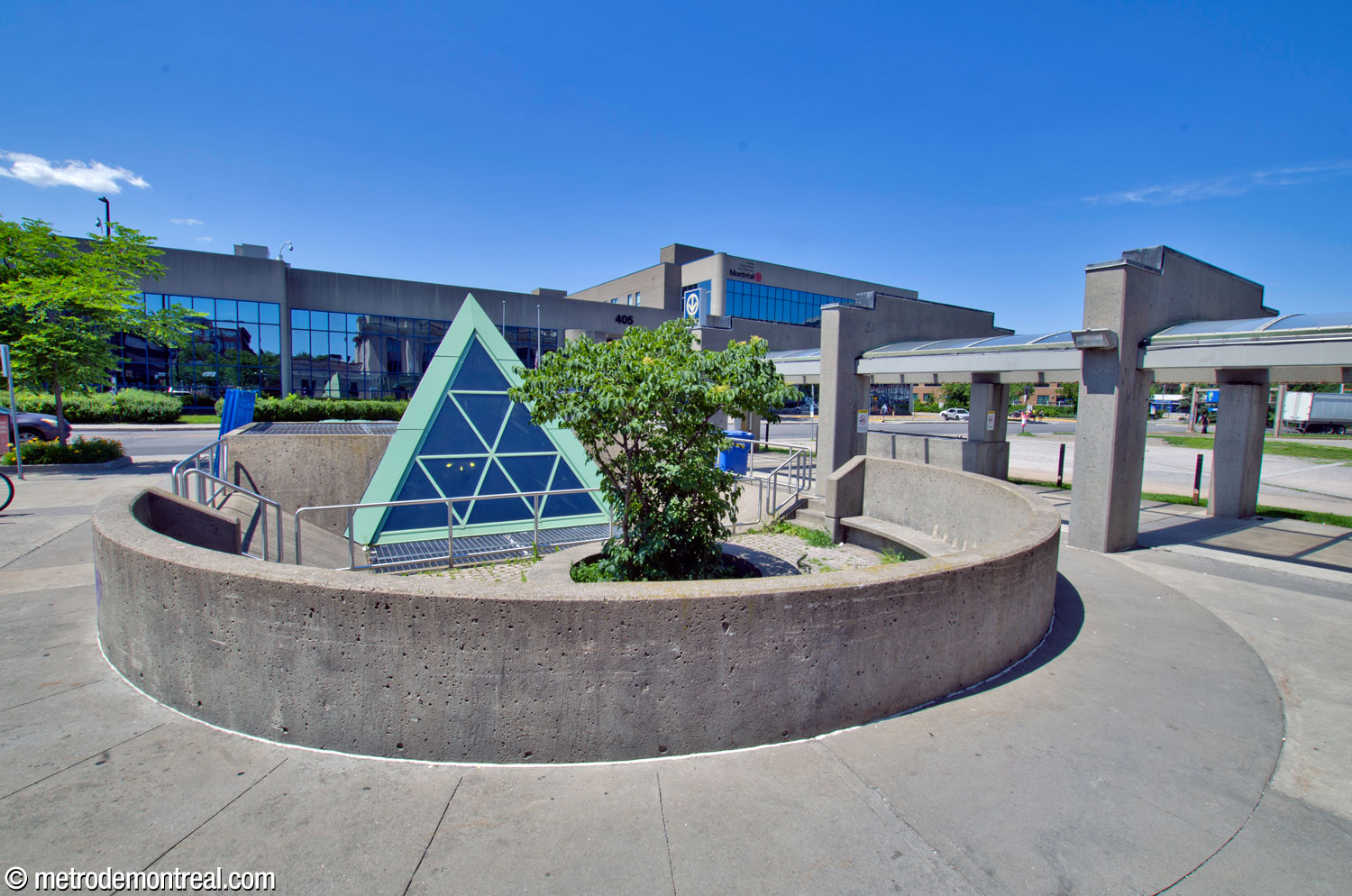 Un espace circulaire surbaissé devant la façade nord de la station incorpore la lanterne triangulaire du puits de lumière, avec un bac à plantes et des bancs.