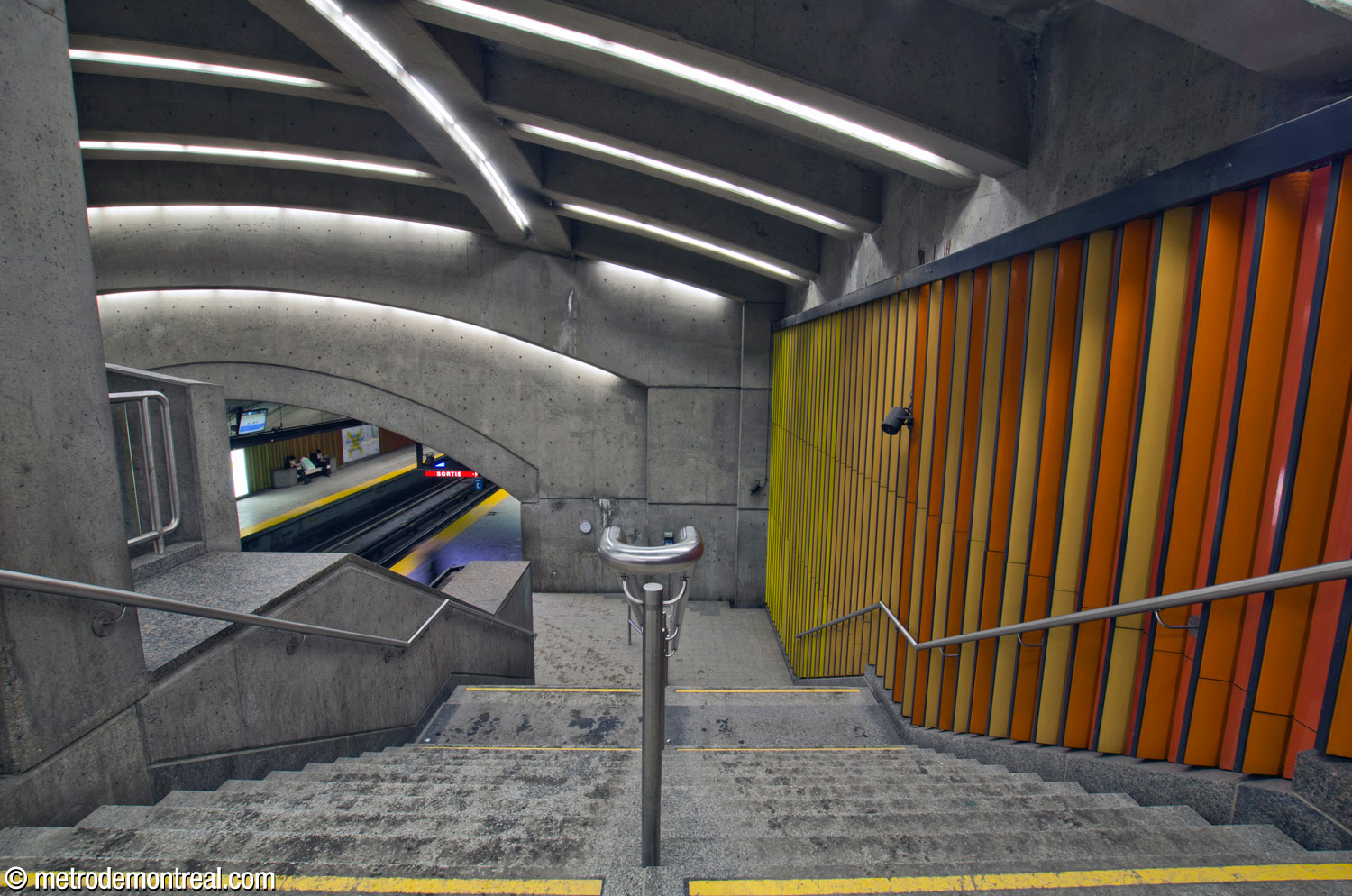 Vue vers le bas de l'escalier entre la mezzanine et le quai Saint-Michel. La frise murale de Huguette Desjardins pare le mur à droite.
