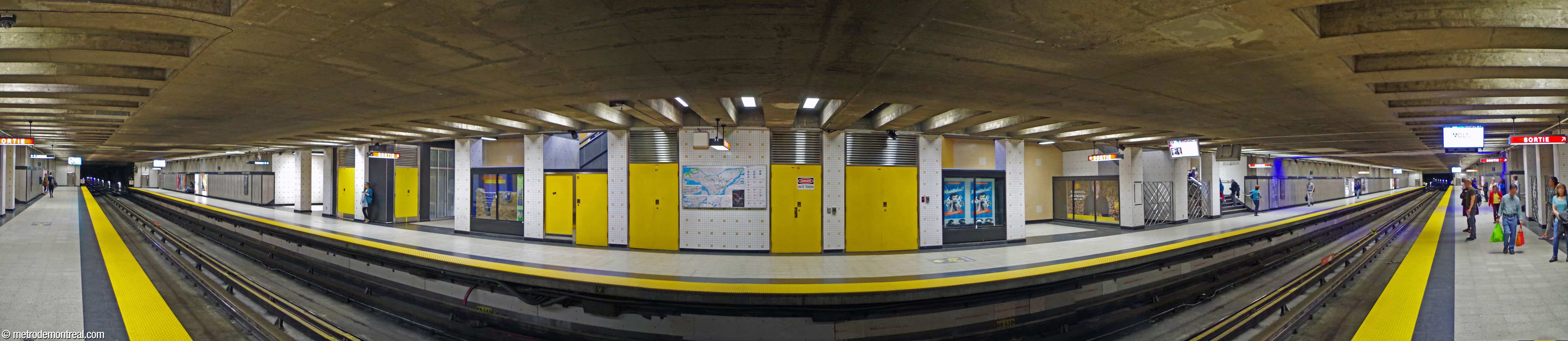 Vue panoramique des quais, construits en tranchée. La partie centrale est revêtue de carreaux beiges et couleur caramel; les portes des locaux techniques sont jaune vif. Les murs aux extrémités des quais sont parés de panneaux d'acier inoxydable texturé.