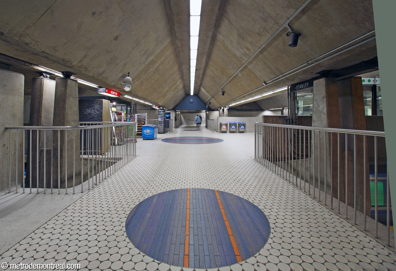 La salle de contrôle à l'extrémité ouest de la mezzanine; la barrière de perception se trouve à droite. Des passerelles au nord et au sud de la mezzanine la relient aux sorties Peel Ouest et Stanley respectivement. Les sorties définissent des travées alignées avec les caissons triangulaires du plafond. Au centre, l'un des grands cercles de Jean-Paul Mousseau, entre deux autres plus petits.