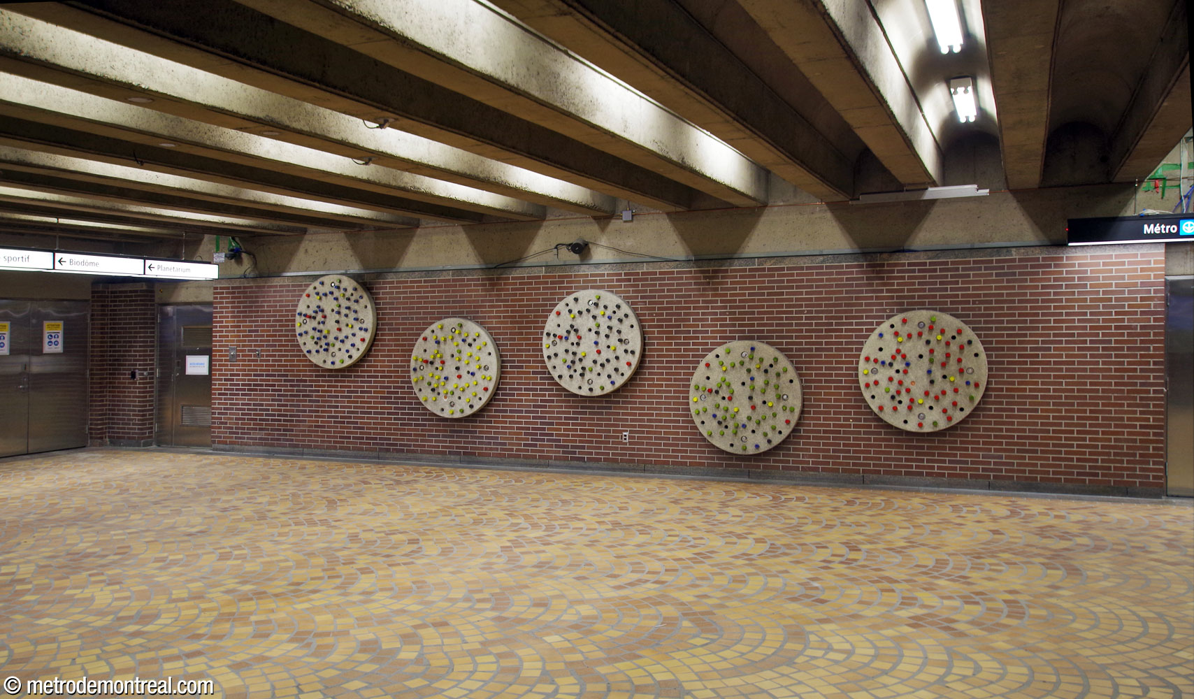 Marcel Raby's installation of five concrete disks in the position of the Olympic rings, studded with glazed ceramic knobs in the Olympic colours, located on the ticket hall level facing the Olympic Stadium access.