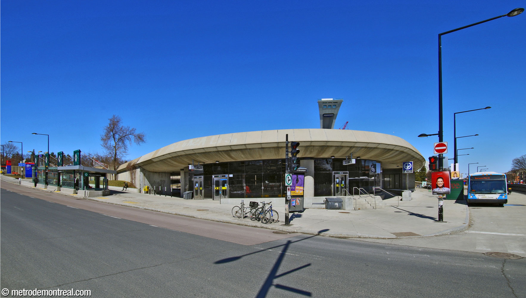 The curved façade of the Pie-IX Est entrance, integrated into the esplanade of the Olympic Stadium. Exits open onto Boulevard Pie-IX (left) and Avenue Pierre-De Coubertin (right). A few metres away from the exit is the Pierre-De Coubertin station of the SRB Pie-IX (far left).
