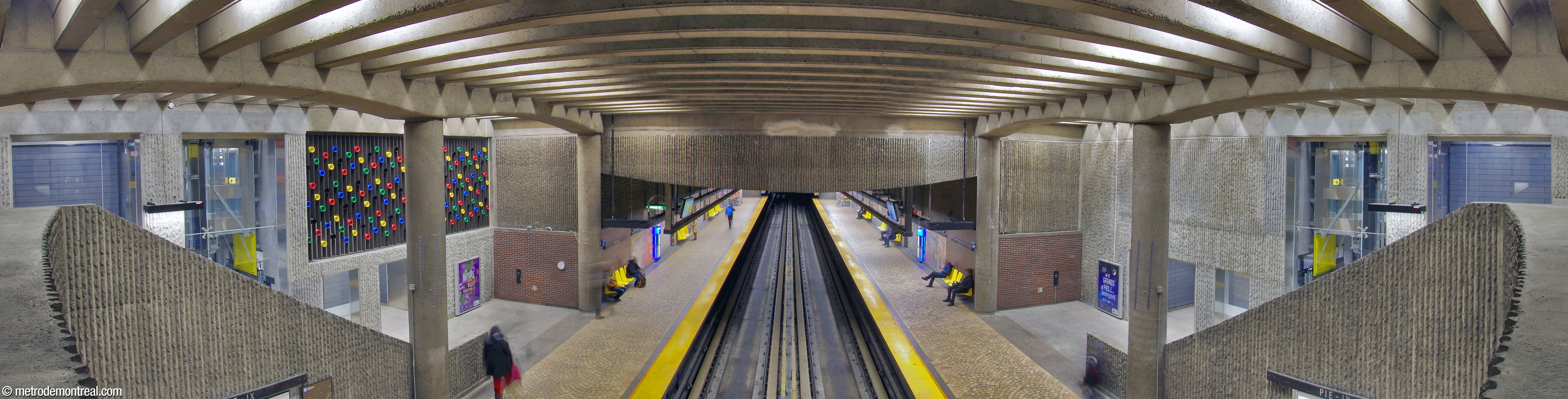 View of the eastern end of the trainroom, showing the unusual reversed-arch shape of the ceiling over the end of the platforms. The elevators to the platform are seen on either side, adjacent to the staircases; Marcel Raby's sculptural grille is on the left, above the Angrignon platform.