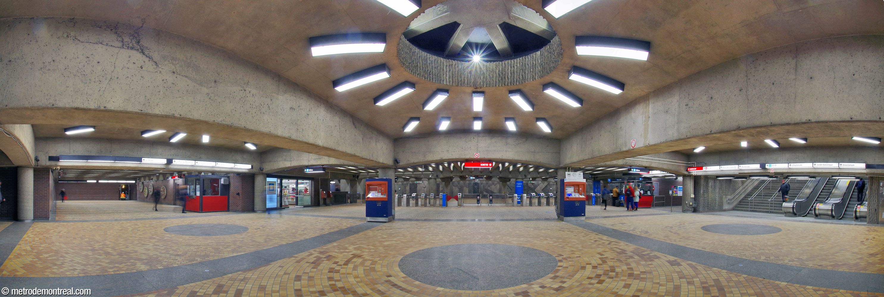 The vast concourse connects the various accesses—from the stadium (left), the Pie-IX Est entrance (right), and the hallway from the Pie-IX Ouest entrance (centre-right, next to the ticket booth)—and directs the passenger flows along the whole length of the ticket barrier. Three circular openings in the ceiling in this area, originally intended as skylights, are ringed by light fixtures and copied by tiled circles on the floor. This panorama was taken before the installation of Francis Montillaud’s work Point de mire in these openings.
