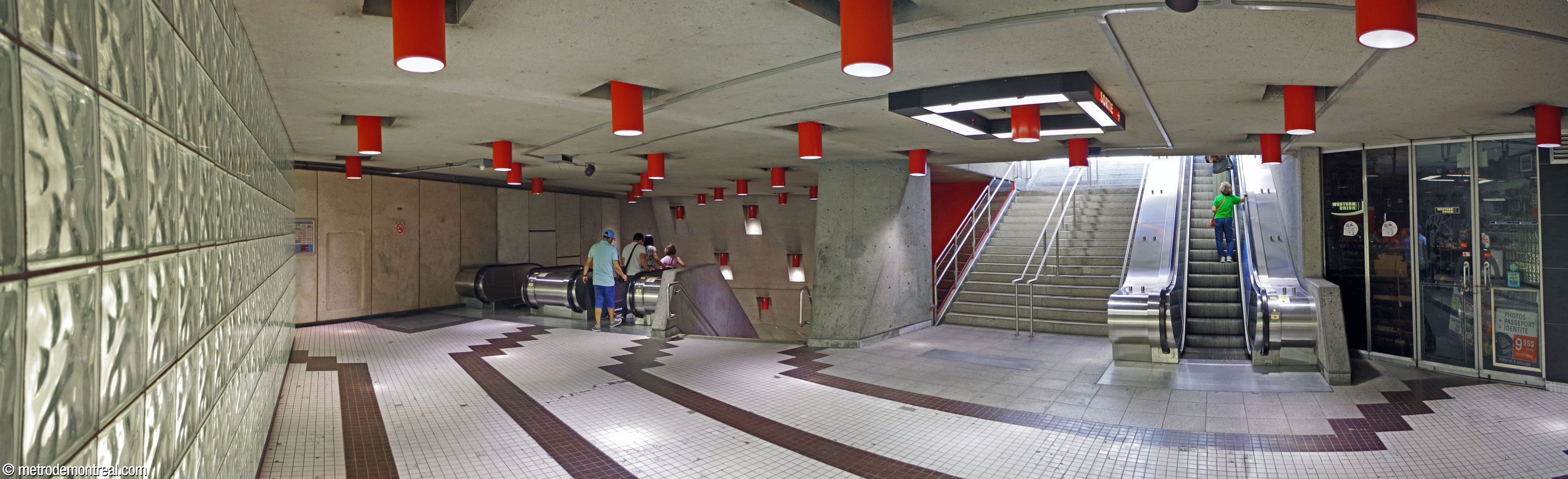 Le palier situé sous l'édicule Van Horne. De gauche à droite, un mur de brique rétroéclairé, la tête des escaliers vers la billetterie, les escaliers vers le rez-de-chaussée et un local commercial.