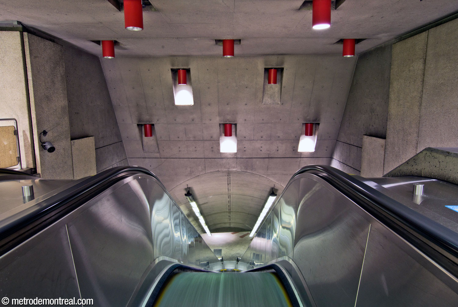 La tête de l'escalier principal au niveau de la billetterie nord. Au plafond, on remarque les luminaires rouges de forme cylindrique.