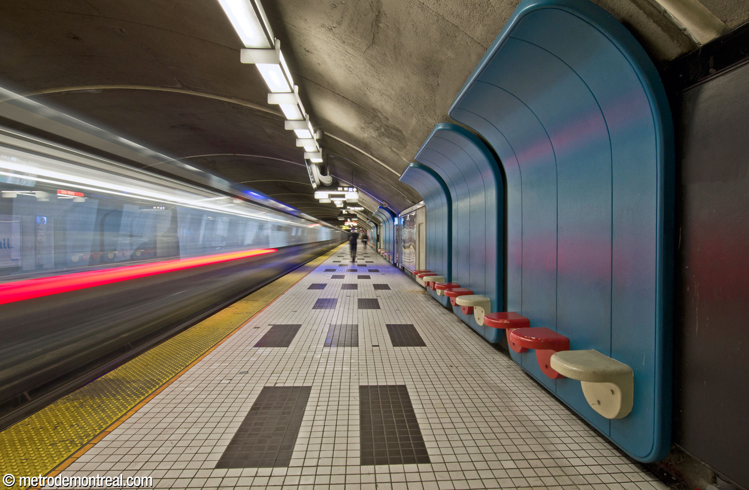 Les dossiers courbes des sièges modulaires, bleus dans la moitié nord de la station, épousent la courbe de la voûte au-dessus du quai Côte-Vertu. On remarque le motif fort en noir et blanc au sol.