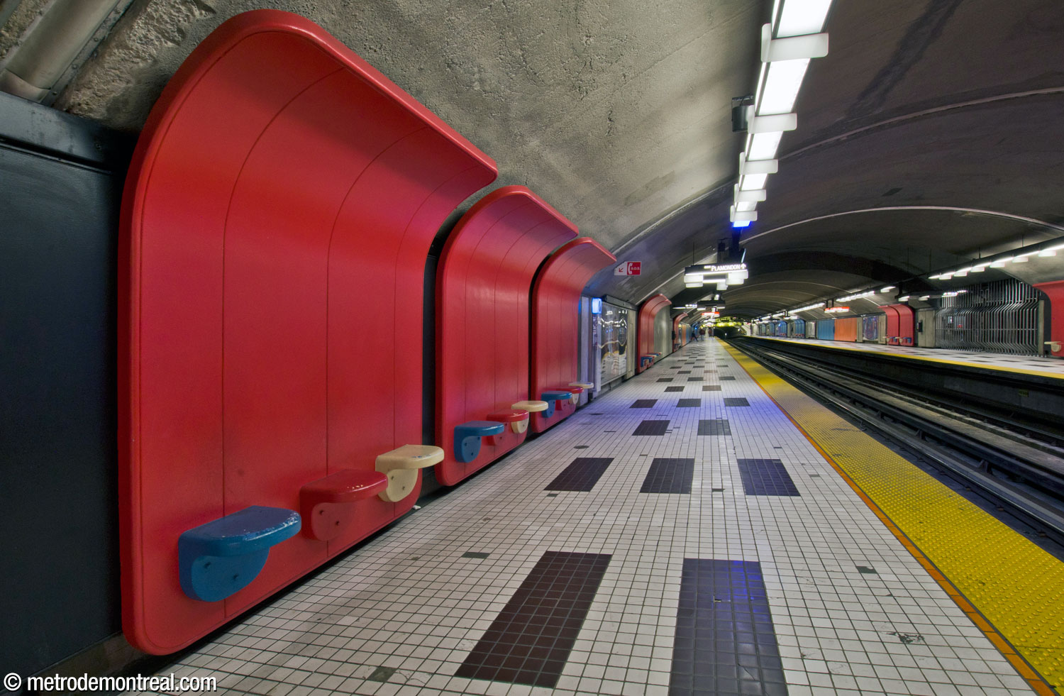 Les dossiers courbes des sièges modulaires, rouges dans la moitié sud de la station, épousent la courbe de la voûte au-dessus du quai Montmorency. On remarque le motif fort en noir et blanc au sol.